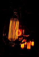Detailed close-up of vintage-style Edison light bulbs glowing with a warm orange hue. The filaments inside the bulbs are intricately visible, creating a sense of warmth and nostalgia in the dimly lit environment.