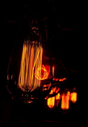Detailed close-up of vintage-style Edison light bulbs glowing with a warm orange hue. The filaments inside the bulbs are intricately visible, creating a sense of warmth and nostalgia in the dimly lit environment.