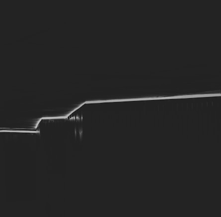 A minimalistic black and white photograph featuring a diagonal line created by lighting or shadow, dividing the image. The simplicity of the composition emphasizes geometric shapes and abstract forms.