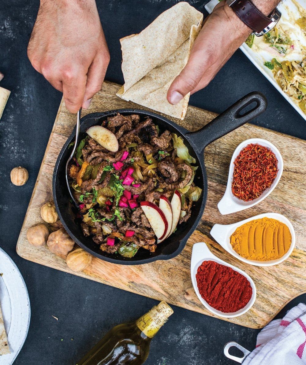 person holding black frying pan with cooked food