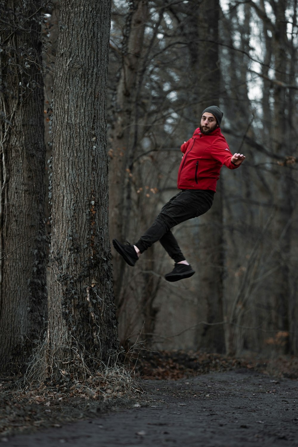 uomo in felpa con cappuccio rossa e pantaloni neri che salta sul tronco d'albero durante il giorno