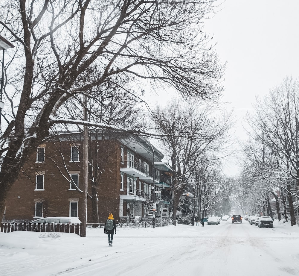 person in black jacket walking on snow covered road during daytime