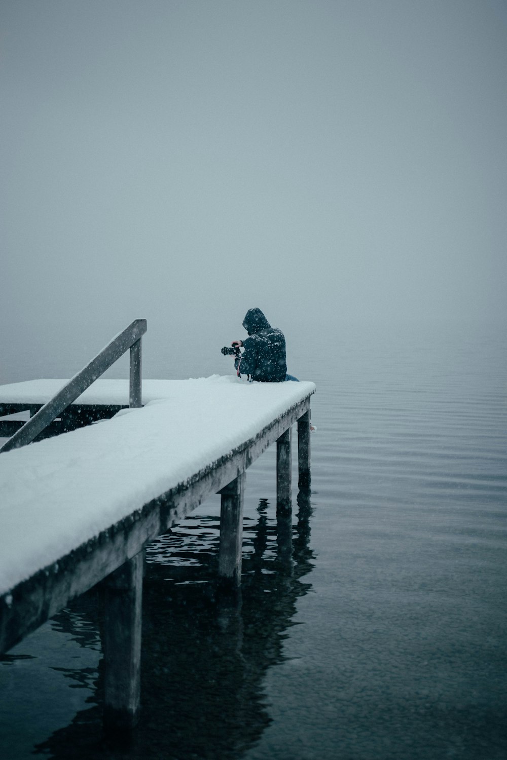man in black jacket sitting on wooden dock
