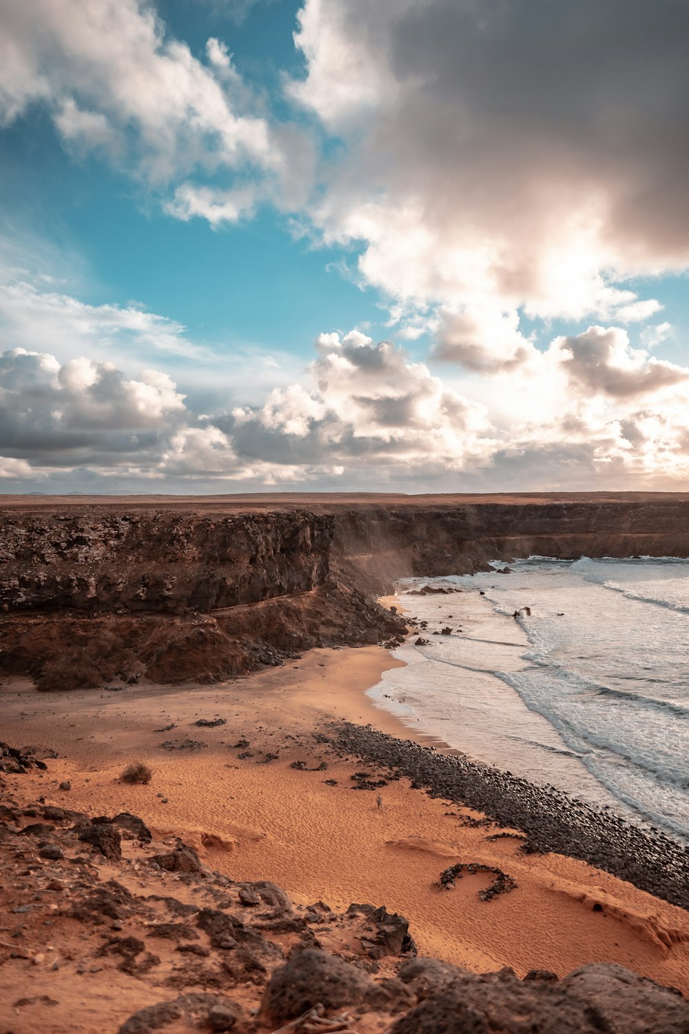 brown field near body of water under blue and white cloudy sky during daytime