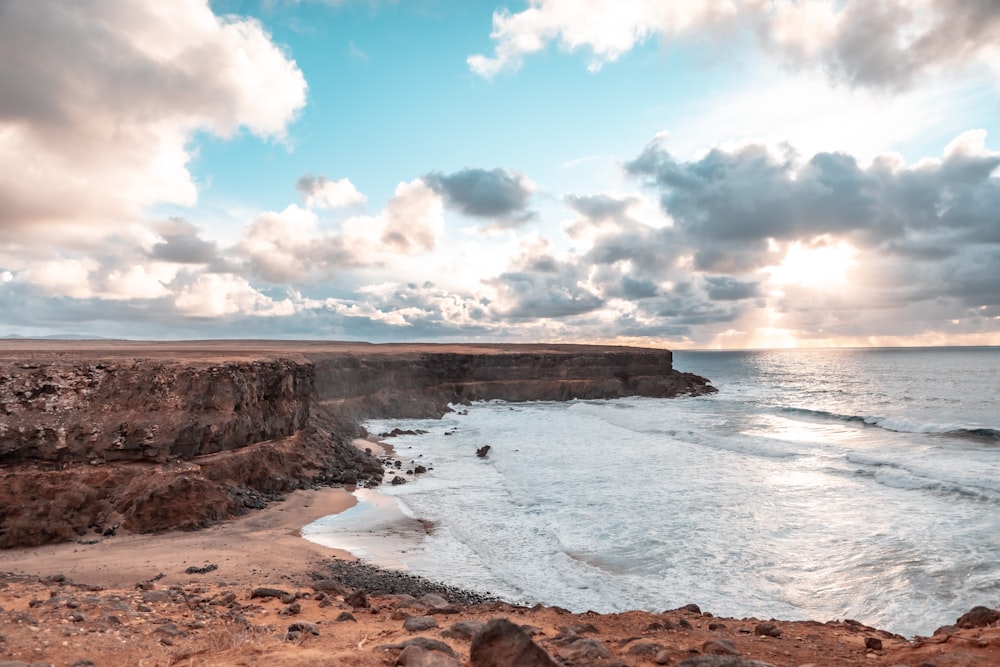 brown rock formation near body of water under blue and white cloudy sky during daytime