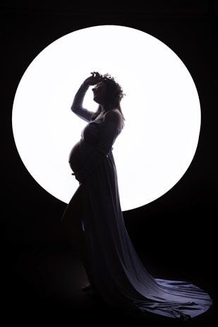 A solo shot of a mom-to-be standing tall, her silhouette outlined by soft natural light and a simple backdrop.