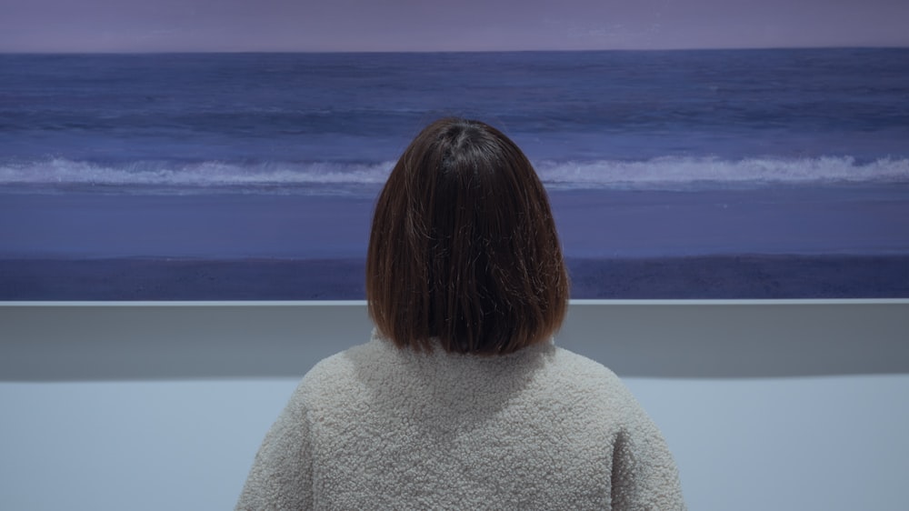 woman in gray sweater standing near body of water during daytime