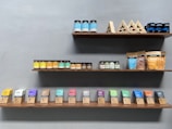 Shelves displaying a variety of packaged food products, including jars of peanut butter and almond butter, and assorted boxes and bags of cacao butter and sweeteners. The arrangement is neat and organized by product type and color, with a minimalist design.