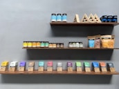 Shelves displaying a variety of packaged food products, including jars of peanut butter and almond butter, and assorted boxes and bags of cacao butter and sweeteners. The arrangement is neat and organized by product type and color, with a minimalist design.