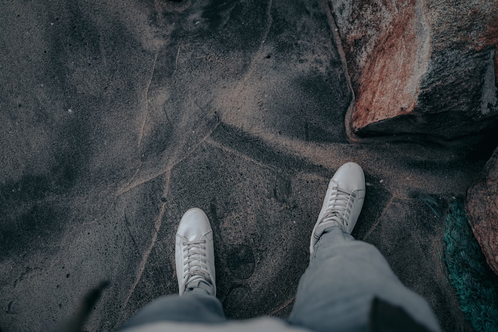 person in white sneakers standing on brown sand