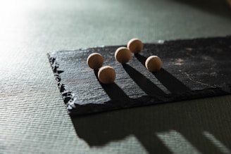 Five small spherical objects are placed on a rectangular piece of slate. The light creates elongated shadows, emphasizing the rough texture of the slate and the smooth surfaces of the spheres.