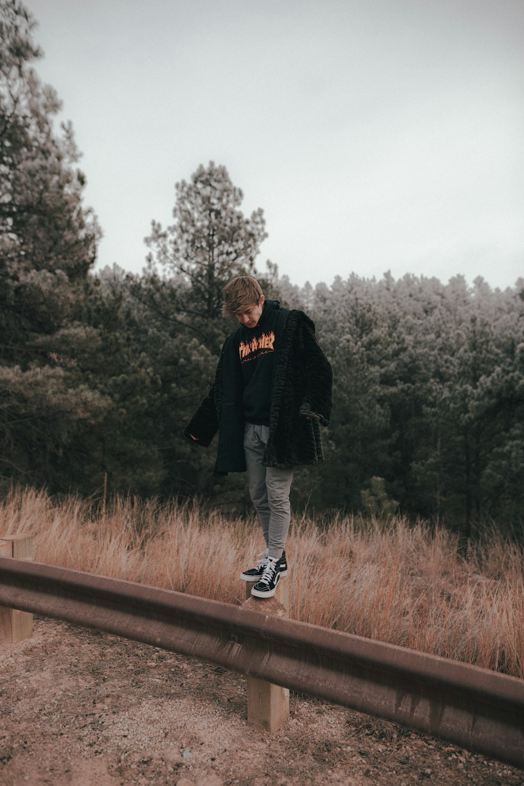 man in black jacket and gray pants standing on brown wooden rail during daytime