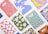 A collection of colorful notebooks arranged on a white surface. Each notebook features a unique and vibrant abstract design, including patterns of bananas, fried eggs, milk splashes, and other geometric shapes.
