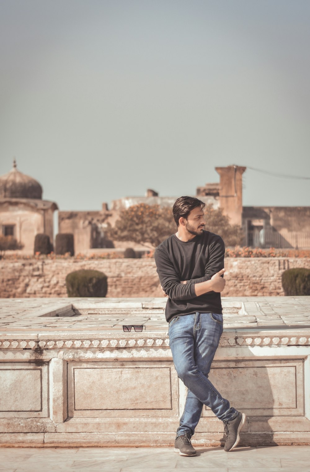 man in black and white striped shirt and blue denim jeans sitting on concrete fence during