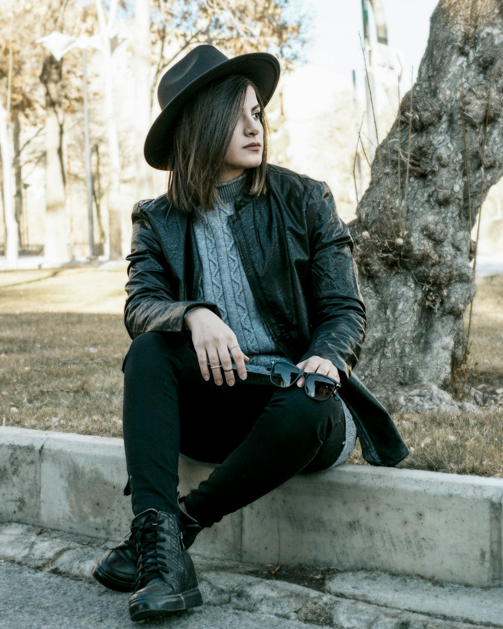woman in black leather jacket and black pants sitting on concrete bench during daytime
