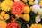 A vibrant bouquet of flowers featuring prominently blooming red roses, surrounded by clusters of bright yellow chrysanthemums and soft white flowers tinged with purple edges. The arrangement is lush and full, set against a backdrop of rich green foliage.