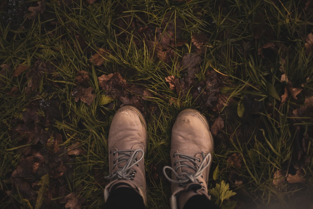 person wearing brown and white shoes standing on brown dried leaves