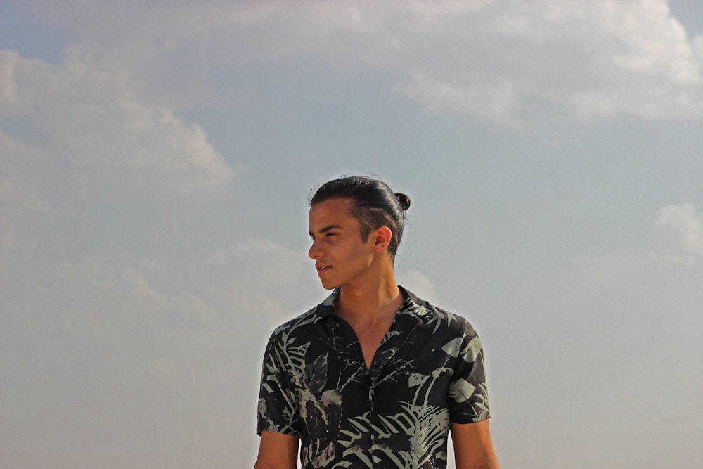 man in black and white floral button up shirt standing under white clouds during daytime