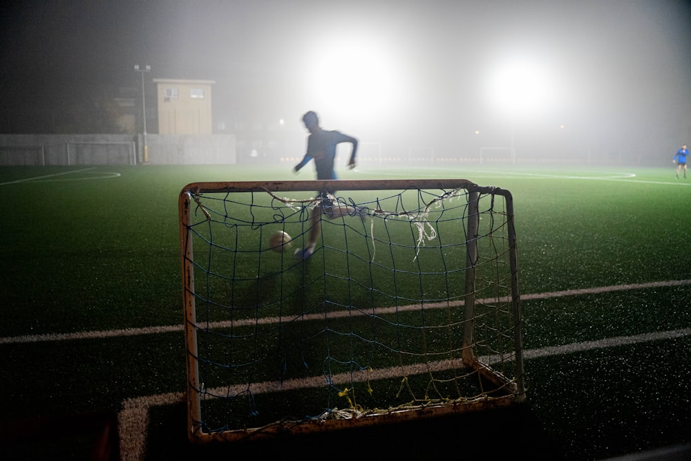 man in black shirt standing on soccer goal net during night time