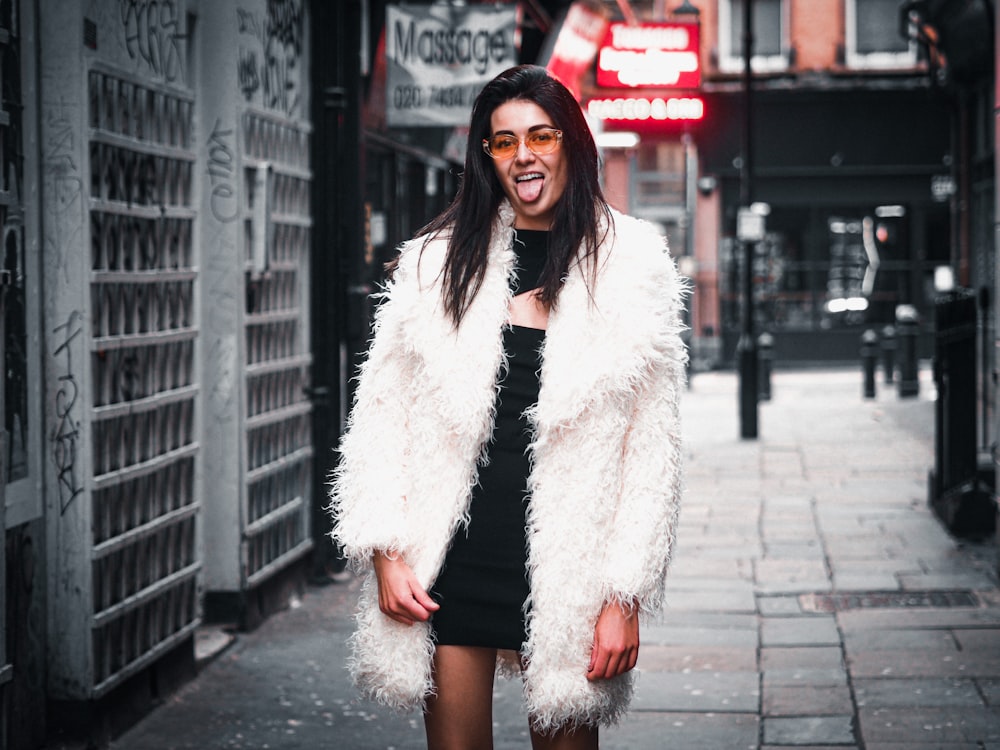 woman in white fur coat standing on sidewalk during daytime