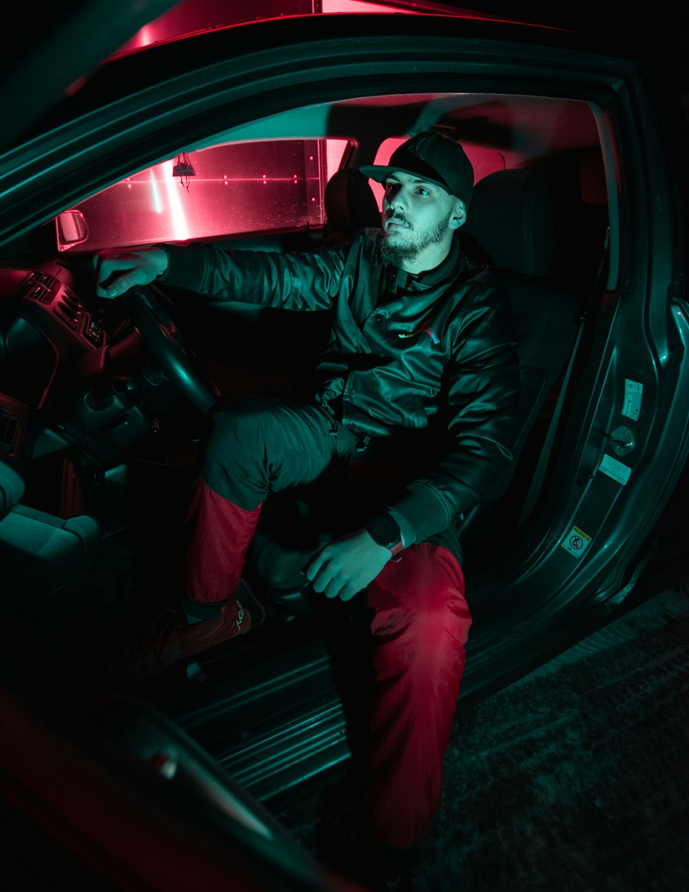 man in black leather jacket and red pants sitting on car seat