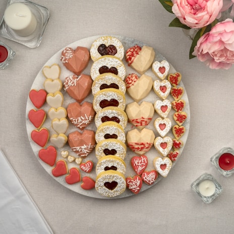 An assortment of custom cookies shaped like flowers and hearts in soft beige and pink tones displayed on a rustic wooden table.
