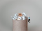 a miniature man standing on top of a pile of toilet paper
