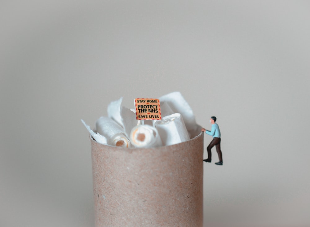 a miniature man standing on top of a pile of toilet paper