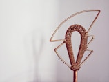 A decorative object made of metal wire, shaped into an abstract design with a central woven section. It is set against a plain background, creating a minimalist effect.
