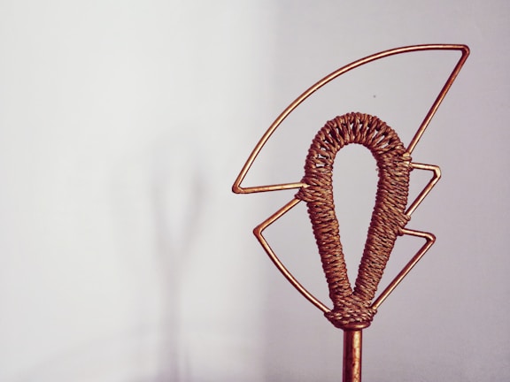 A decorative object made of metal wire, shaped into an abstract design with a central woven section. It is set against a plain background, creating a minimalist effect.
