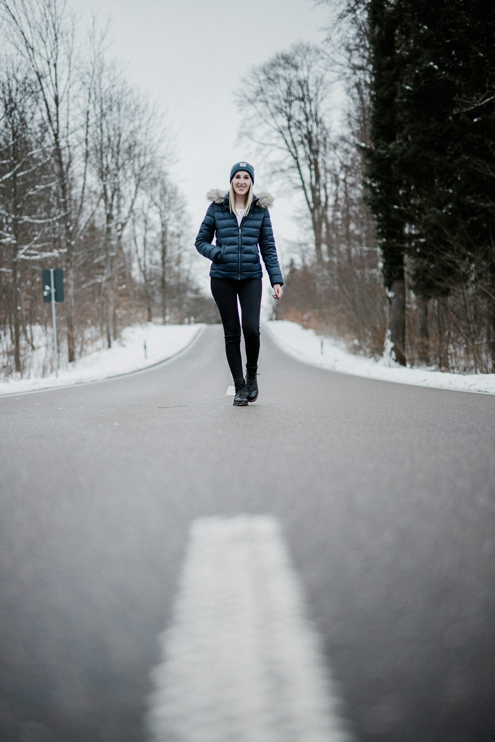 woman in black jacket and black pants standing on snow covered road during daytime