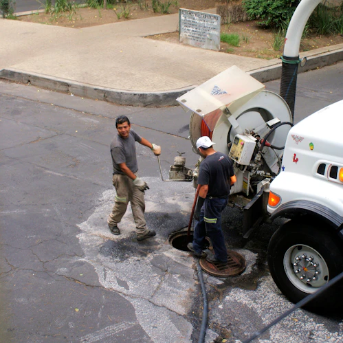 Technician in uniform operating a high-pressure water jet machine for septic tank cleaning in a residential area.