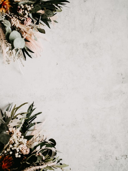 Dark green leaves and various foliage are arranged decoratively in the top left and bottom right corners against a light, textured background.
