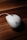 A white computer mouse with a prominent logo is placed on a wooden surface. The lighting highlights the smooth curves and design of the mouse, creating a contrast with the textured background.