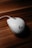 A white computer mouse with a prominent logo is placed on a wooden surface. The lighting highlights the smooth curves and design of the mouse, creating a contrast with the textured background.