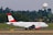 A commercial airplane with the Austrian Airlines logo is taxiing on a runway with a backdrop of trees and a radar tower in the background. The aircraft is white with red accents, visible registration number OE-LDG, and features distinct branding on the fuselage and engine.
