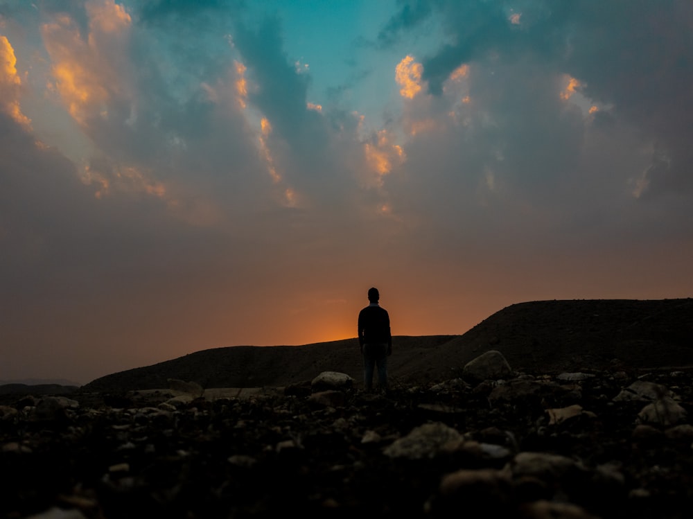 silhouette of man standing on rock during sunset