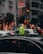 A busy urban street scene featuring a traffic police officer in a reflective vest directing vehicles. Tall buildings and storefronts line the street, with pedestrians walking by. Cars are stopped, and the street is bustling with activity. A sign for Kolan International Hospital is visible above.