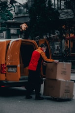 man in red jacket standing beside orange van during daytime