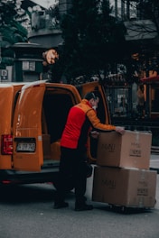 man in red jacket standing beside orange van during daytime