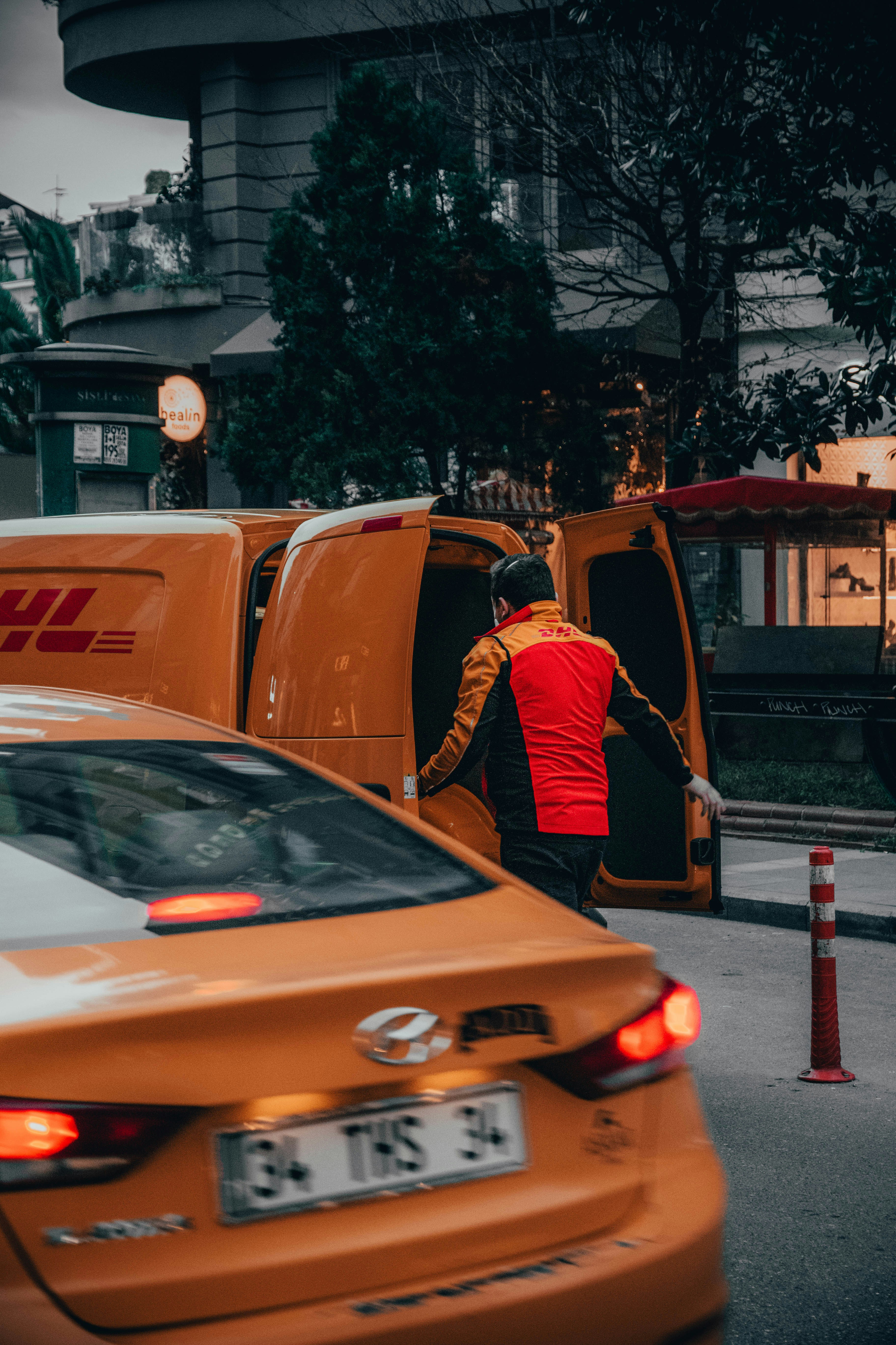 man in black jacket standing beside orange car during daytime