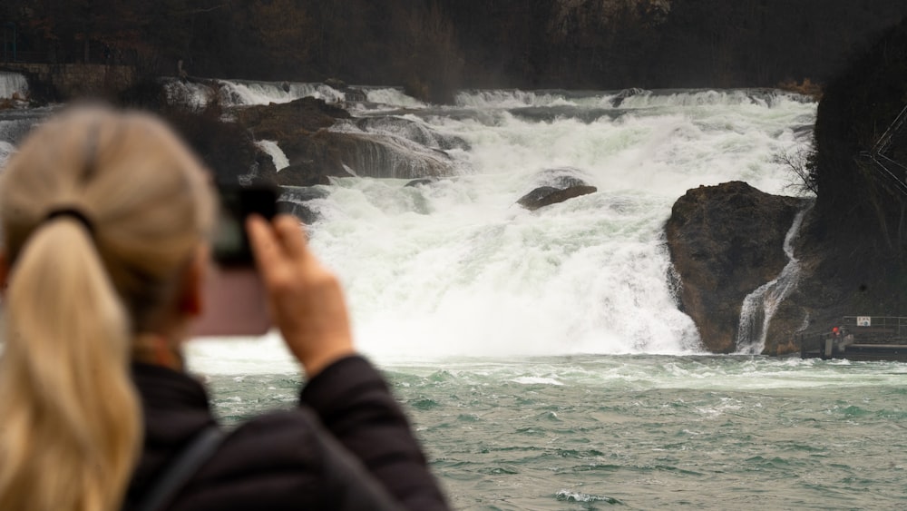 pessoa em jaqueta preta tirando foto de cachoeiras durante o dia