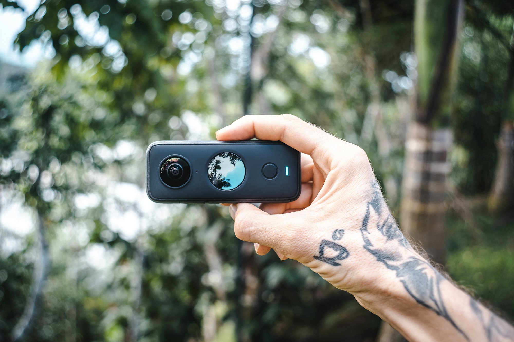 A cameraman is holding up an Insta360 ONE X2 360 action camera outdoor