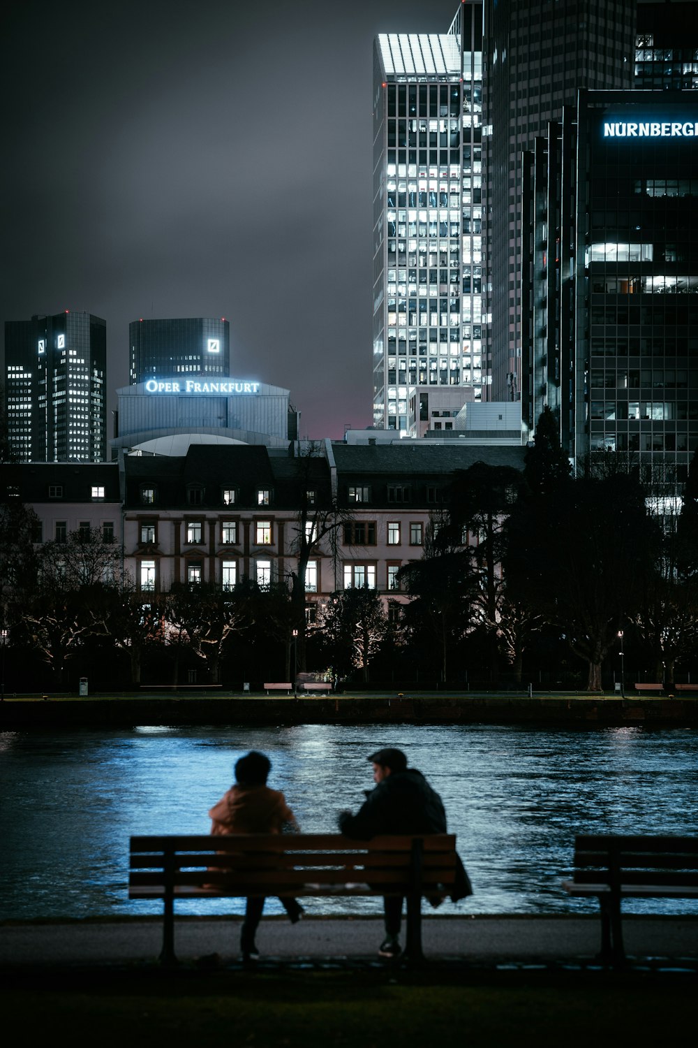 man and woman sitting on bench near body of water during night time