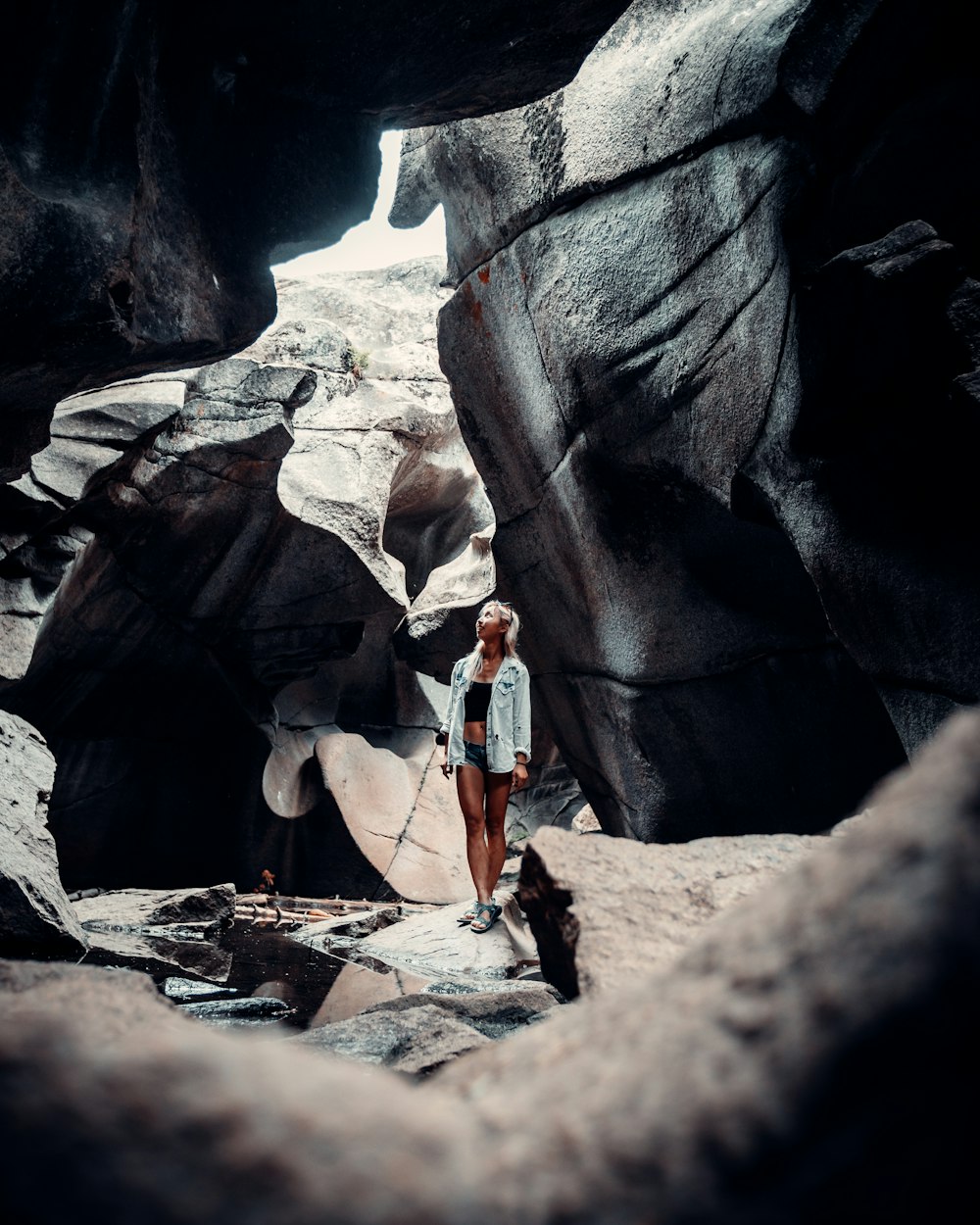 woman in white tank top and blue denim shorts standing on rocky ground