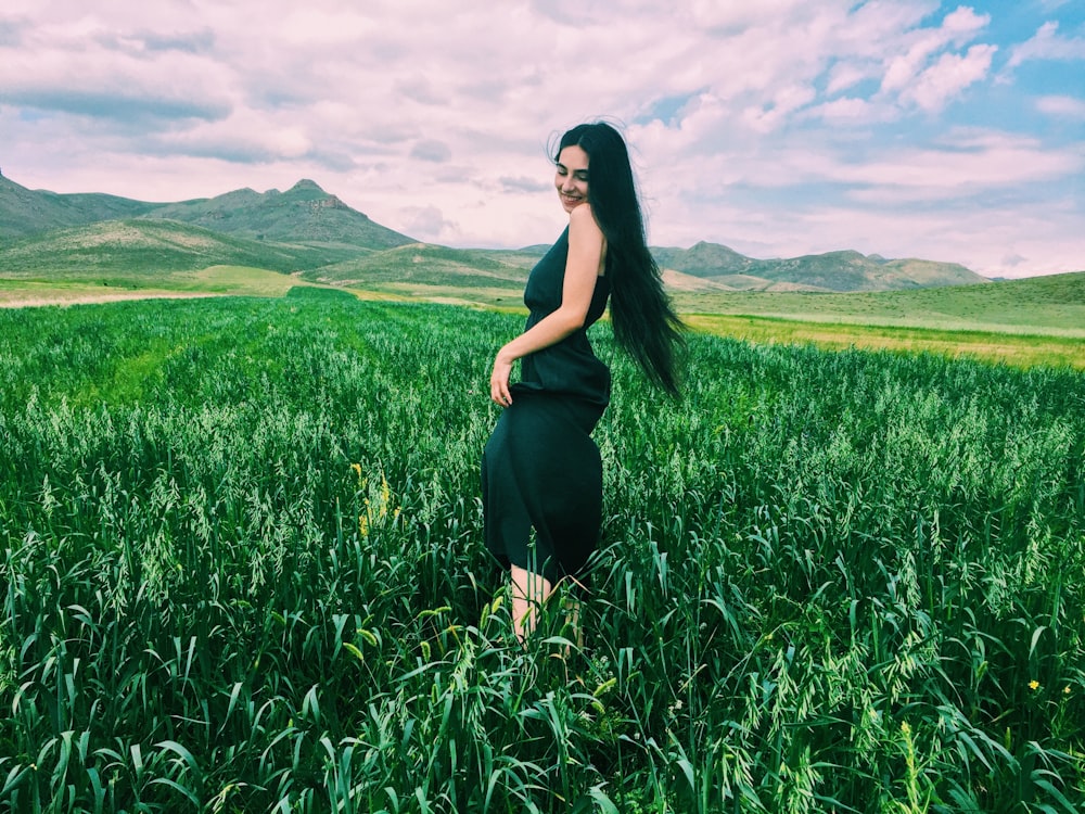 femme en robe noire debout sur le champ d’herbe verte pendant la journée