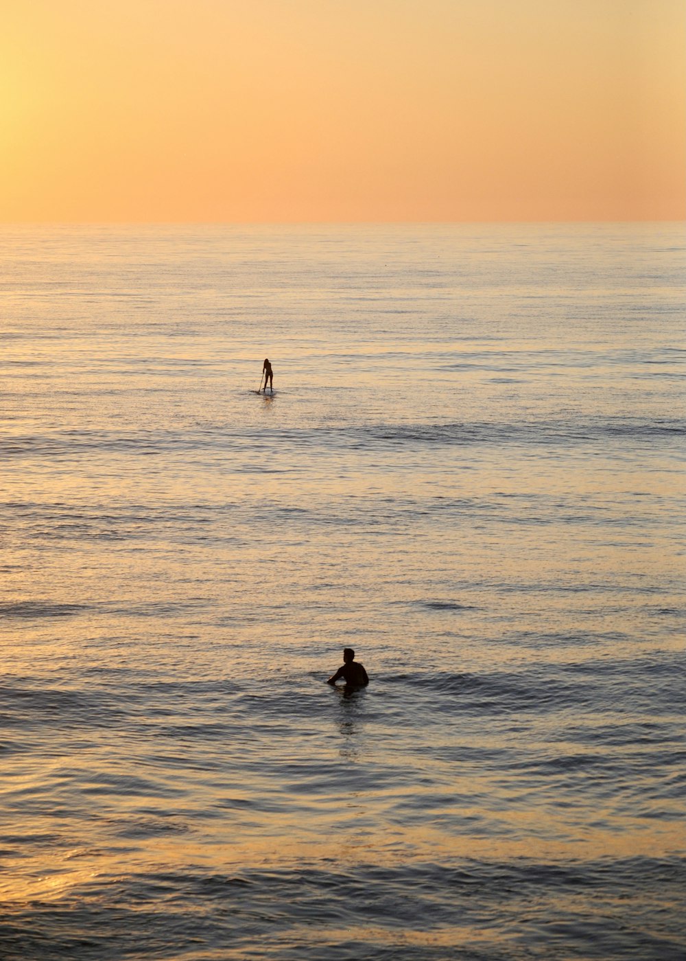 2 people swimming on sea during sunset