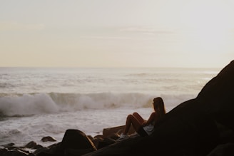 woman in black tank top sitting on rock near sea during daytime