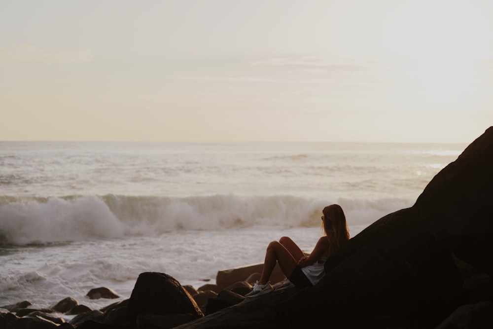 femme en débardeur noir assise sur un rocher près de la mer pendant la journée