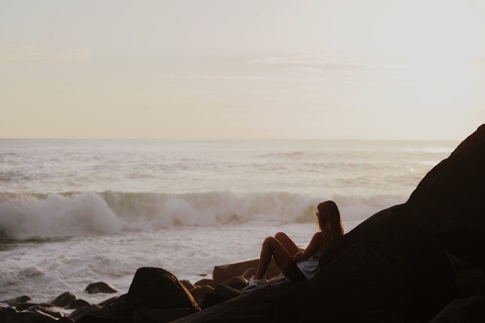 woman in black tank top sitting on rock near sea during daytime